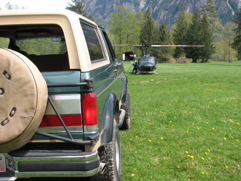 1990 Ford Bronco - A green Ford Bronco is parked in a field with a helicopter in the background.