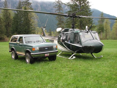 1990 Ford Bronco - A green 1990 Ford Bronco is parked on a grassy field next to a sheriff's department helicopter.