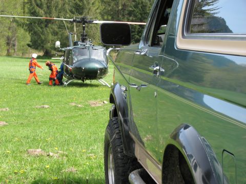1990 Ford Bronco - A green SUV is parked in a field near a helicopter and two individuals in orange uniforms.