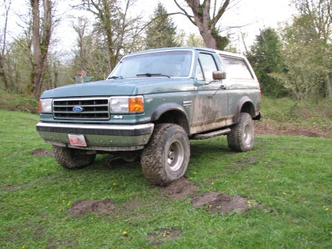 1990 Ford Bronco - 1990 Ford Bronco with off-road tires on a muddy field.
