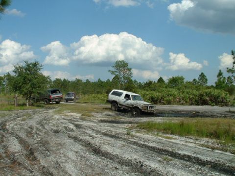 1992 Ford Bronco - Several vehicles navigate a muddy off-road course under a cloudy sky.