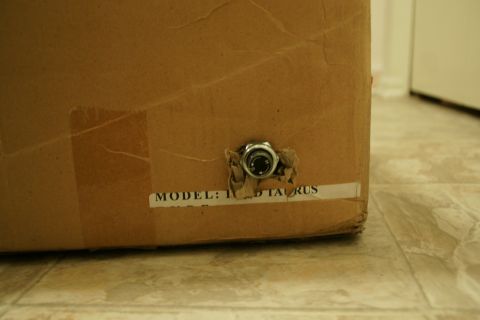 1995 Ford Taurus - A cardboard box has a label that reads 'MODEL: 1995 TAURUS' and a small metal fitting is attached to its side.