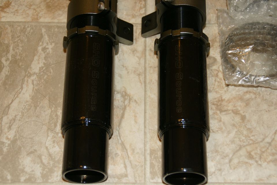 Two black coilover suspension units with 'SHO Source' visible on the side