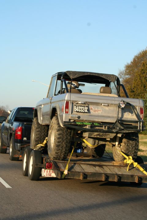 1982 Ford Bronco - A silver Ford Bronco is transported on a trailer behind a black truck on a highway.