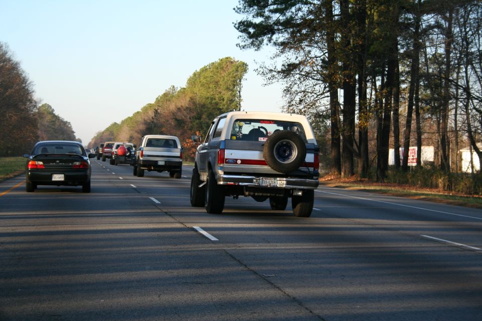Ford Bronco driving on highway, spare tire mounted on rear door. Other vehicles in front
