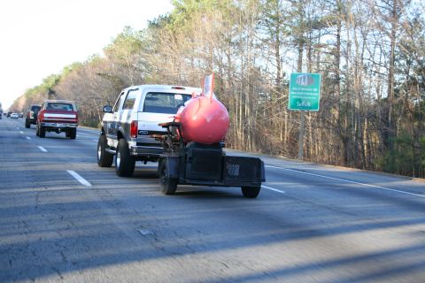 1982 Ford Bronco - A silver Ford Bronco tows a trailer with a large pink object on a highway, with other vehicles visible.