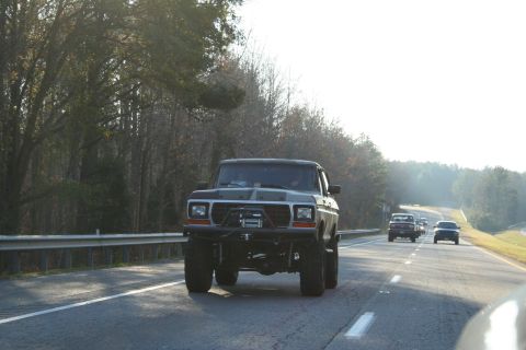 1982 Ford Bronco - A lifted pickup truck is seen driving on a highway with other vehicles in the background.
