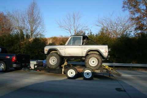 1982 Ford Bronco - A silver Ford Bronco is transported on a trailer towed by a black pickup truck.