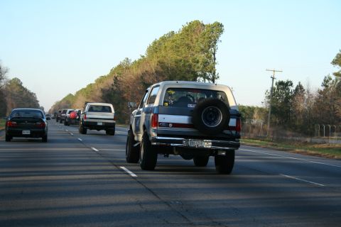1982 Ford Bronco - A line of vehicles travels down a highway under a clear sky.