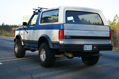 1982 Ford Bronco - This two-tone SUV, likely a Ford Bronco from the early to mid-1990s, is seen from the rear with a roof rack and a personalized Virginia lic…