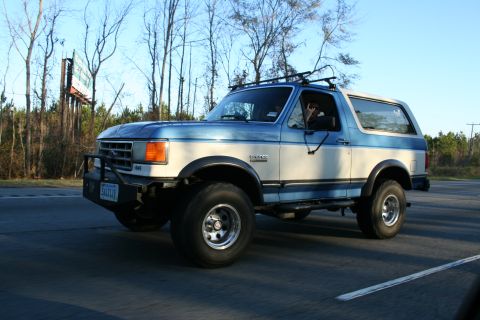 1982 Ford Bronco - This two-tone blue and white Ford Bronco is captured in a 3/4 front view, with a license plate that reads 'SHUTTLE'.