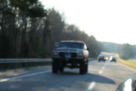 1982 Ford Bronco - A lifted pickup truck drives down the highway, appearing to be from the early 1980s.