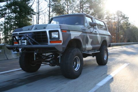 1982 Ford Bronco - This lifted Ford Bronco, painted in camouflage, is seen on the road with an aftermarket bumper and large tires.