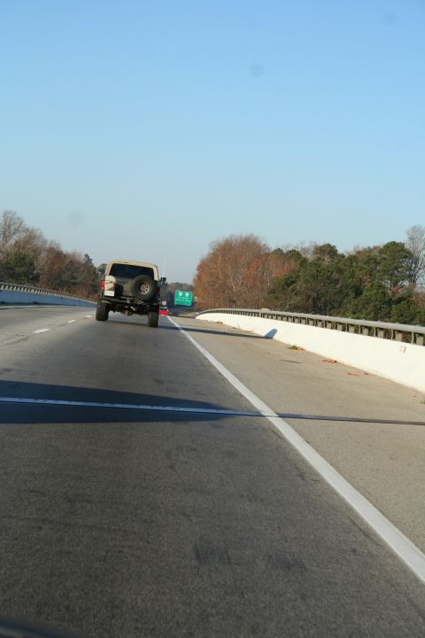 1982 Ford Bronco - A tan SUV, possibly a 1982 Ford Bronco, is seen from behind driving on a highway.