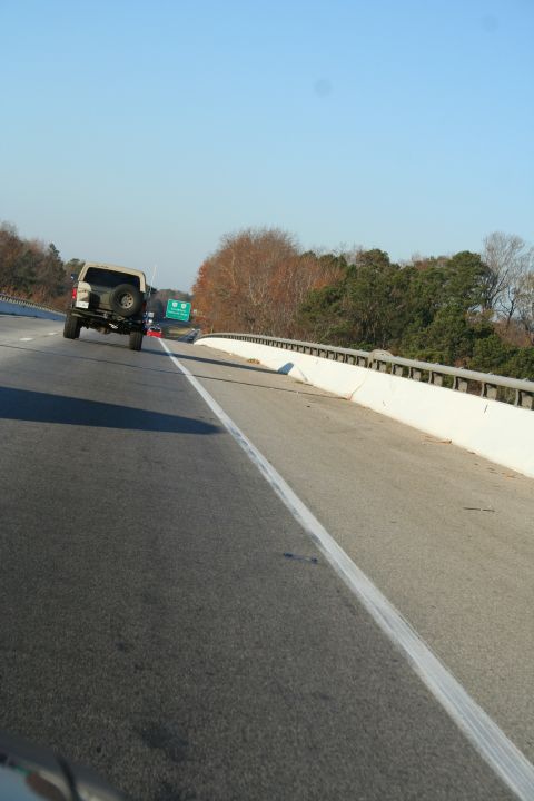 1982 Ford Bronco - A tan Ford Bronco with a spare tire mounted on the rear door drives down a highway.