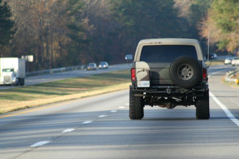 1982 Ford Bronco - This lifted SUV, possibly from the early 1980s, is seen from the rear on a highway, a spare tire and camouflage paint.