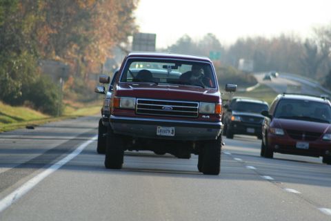 1982 Ford Bronco - A red Ford F-series truck with a 4x4 badge is seen driving on a highway.