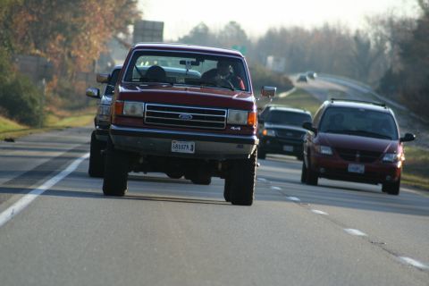 1982 Ford Bronco - A red Ford pickup truck drives down the highway, a grille consistent with the 1987 model year.