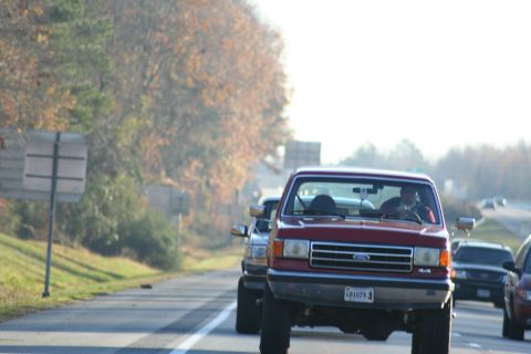 1982 Ford Bronco - Red Ford F-Series truck driving on a highway with other vehicles.