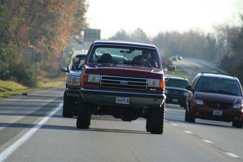 1982 Ford Bronco - A red Ford F-Series truck leads a line of vehicles on a highway during the day.