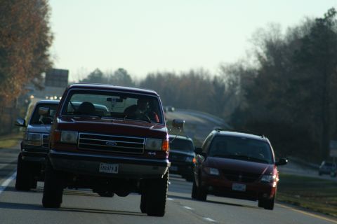 1982 Ford Bronco - A red Ford F-Series truck leads traffic on a highway, with other vehicles visible in the background.