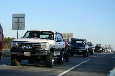 1982 Ford Bronco - Multiple SUVs, including a white Ford Bronco, travel in a convoy on a clear day.
