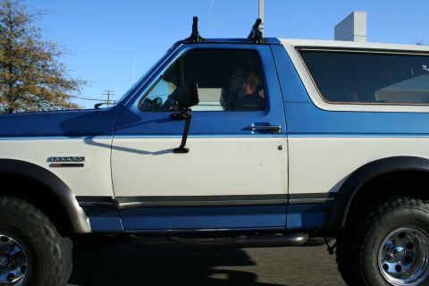 1982 Ford Bronco - The side profile of a two-tone blue and white Ford Bronco shows a "BRONCO" badge on the front fender.