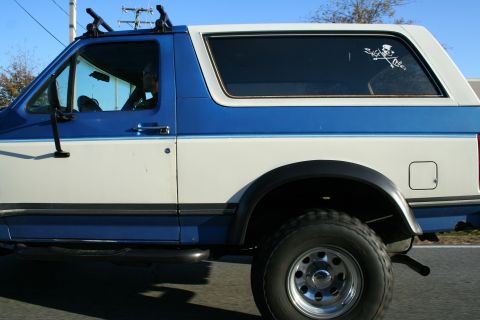 1982 Ford Bronco - This two-tone SUV features a roof rack and a skull and crossbones sticker on the rear window.