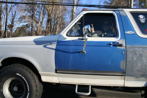 1982 Ford Bronco - Side view of a two-tone blue and white Ford Bronco with a driver giving a thumbs up. The vehicle has aftermarket wheels and appears to be u…