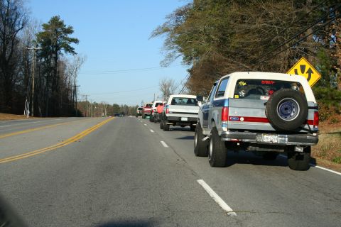 1982 Ford Bronco - A convoy of Ford Broncos, mostly from the late 1980s, travels down a two-lane highway on a clear day.