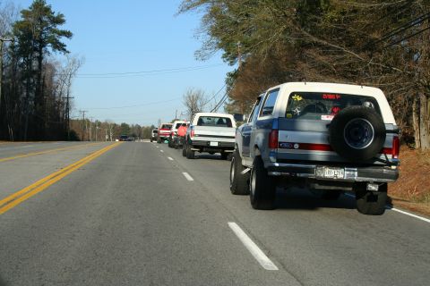 1982 Ford Bronco - A line of trucks and SUVs, including a Ford Bronco, drive down a two-lane road on a clear day.