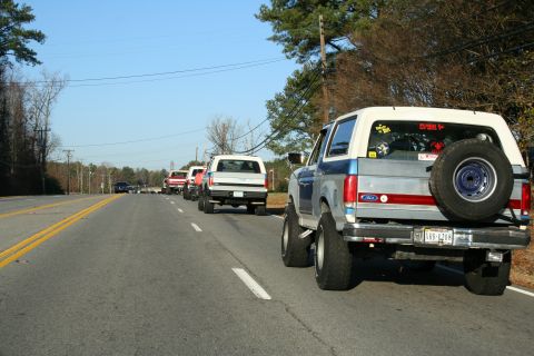 1982 Ford Bronco - A convoy of Ford Broncos, including a blue and silver model with a rear-mounted spare tire, travels down a highway.