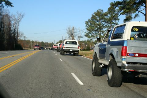1982 Ford Bronco - A line of Ford Broncos drives down a two-lane road on a clear day.