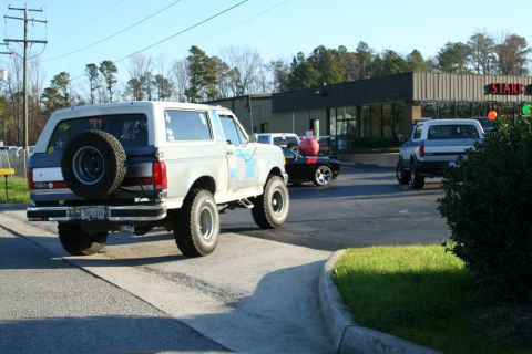 1982 Ford Bronco - A lifted Ford Bronco is seen from the rear, with other vehicles in the background near a commercial building.