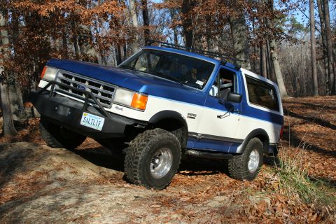 1982 Ford Bronco - This Ford Bronco is navigating a wooded trail with fallen leaves on the ground.