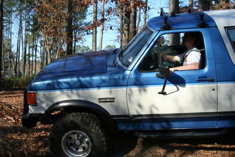 1982 Ford Bronco - Side view of a 1982 Ford Bronco driving through a wooded area.