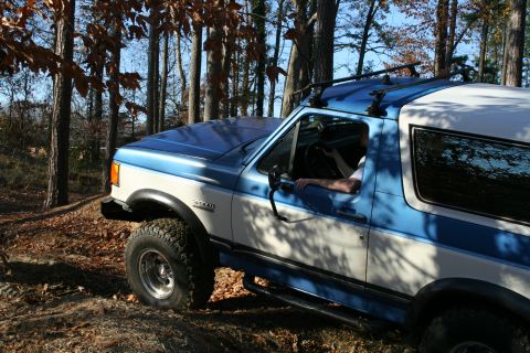 1982 Ford Bronco - This Ford Bronco is equipped with a roof rack and is driving through a wooded area on a sunny day.