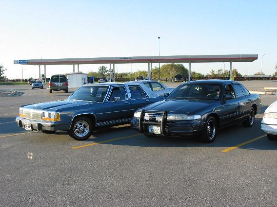 Blue 1980s Ford LTD sedan parked beside a gray Mercury Grand Marquis at a gas station