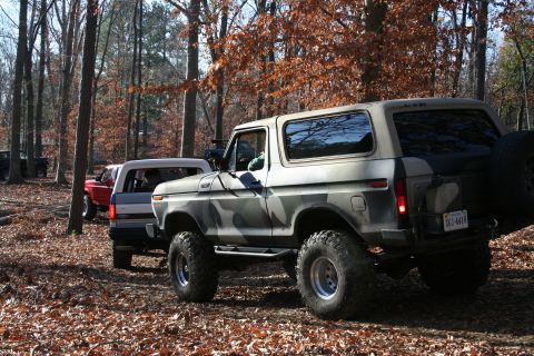 1982 Ford Bronco - A camouflaged 1982 Ford Bronco is seen off-road, with other vehicles in the background.