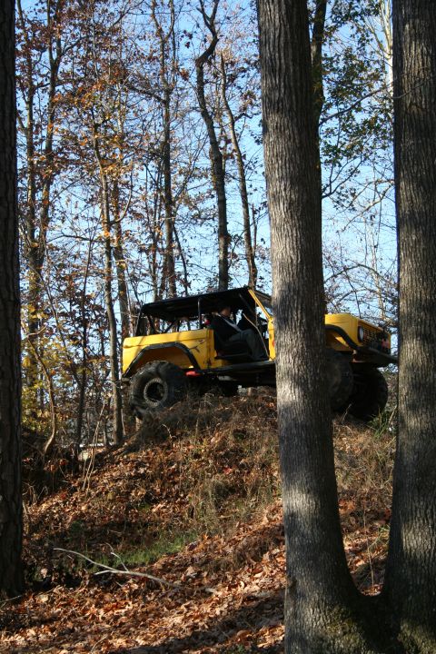 1982 Ford Bronco - A yellow off-road vehicle navigates a steep, leaf-covered incline in a wooded area.