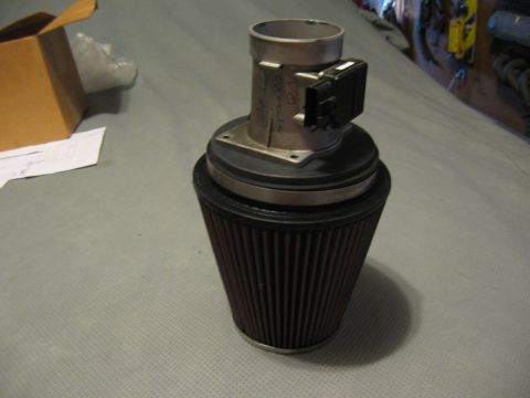 1994 Ford Bronco - A mass air flow sensor is connected to a dark brown conical air filter, resting on a gray surface.