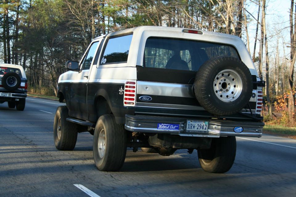 Two Ford Broncos driving on a road, rear view of the closest one. License plate XRW-2942