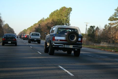 1982 Ford Bronco - A convoy of vehicles, including a Ford Bronco, travels down a highway under a clear sky.