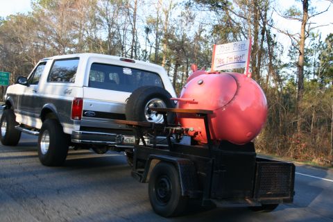 1982 Ford Bronco - Ford Bronco towing a pig-shaped smoker trailer on a road.