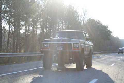 1982 Ford Bronco - A lifted 1978 Ford Bronco is seen driving on a highway, with another vehicle visible ahead.
