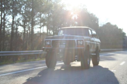 1982 Ford Bronco - This lifted Ford Bronco is driving down a highway with the sun shining brightly.