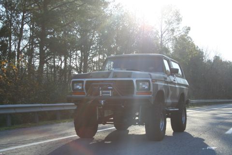 1982 Ford Bronco - This lifted Ford Bronco, likely from 1978, features a winch and camouflage paint, seen driving on a highway.
