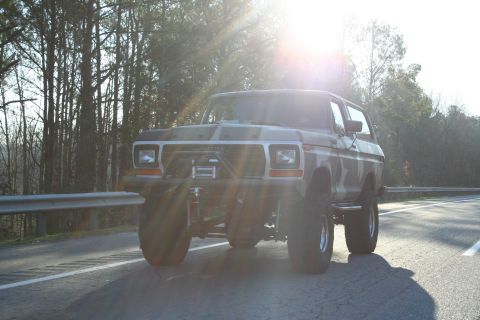 1982 Ford Bronco - This lifted Ford Bronco, likely a 1978 model, is seen driving on a road with trees in the background.