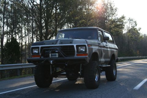 1982 Ford Bronco - A lifted Ford Bronco with a camouflage paint job drives down a road.