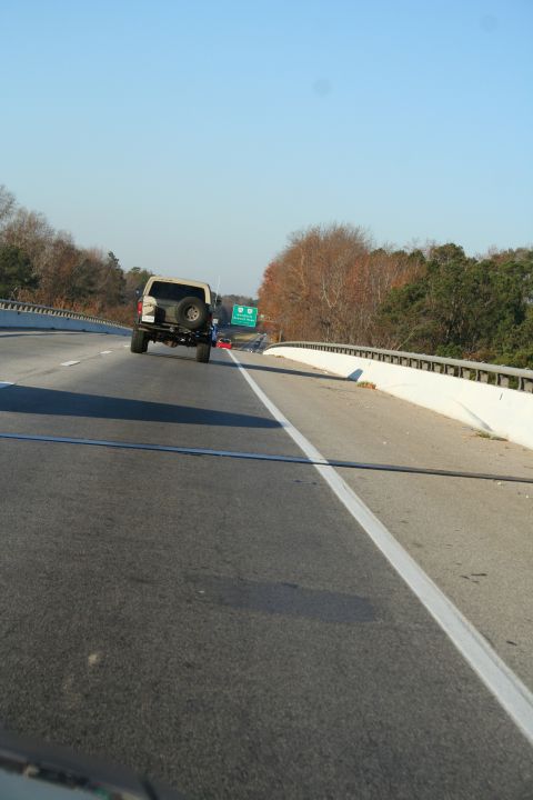 1982 Ford Bronco - A tan Ford Bronco is seen from behind on a highway, with a spare tire mounted on its rear.